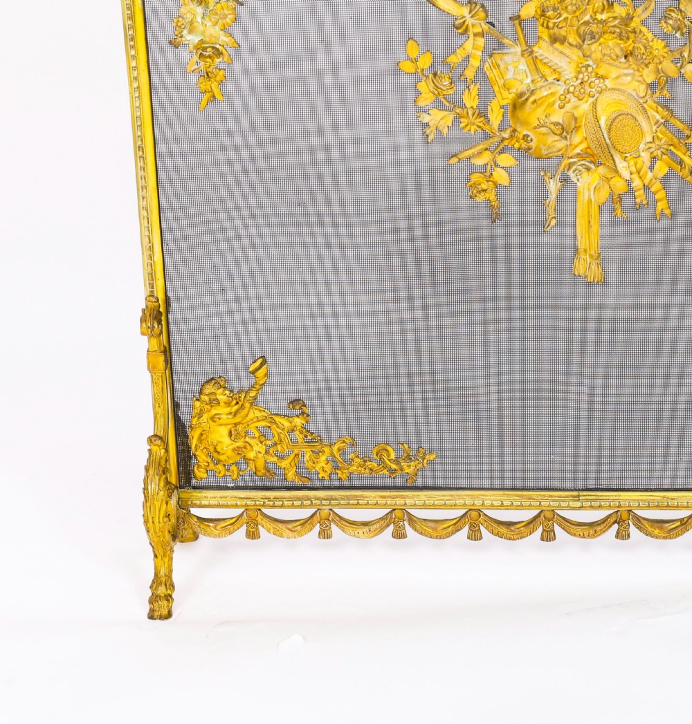 A 19th-century French gilt bronze fire screen featuring a woven mesh panel decorated with central musical trophy motifs, floral garlands, and ribbon swags. View VIII