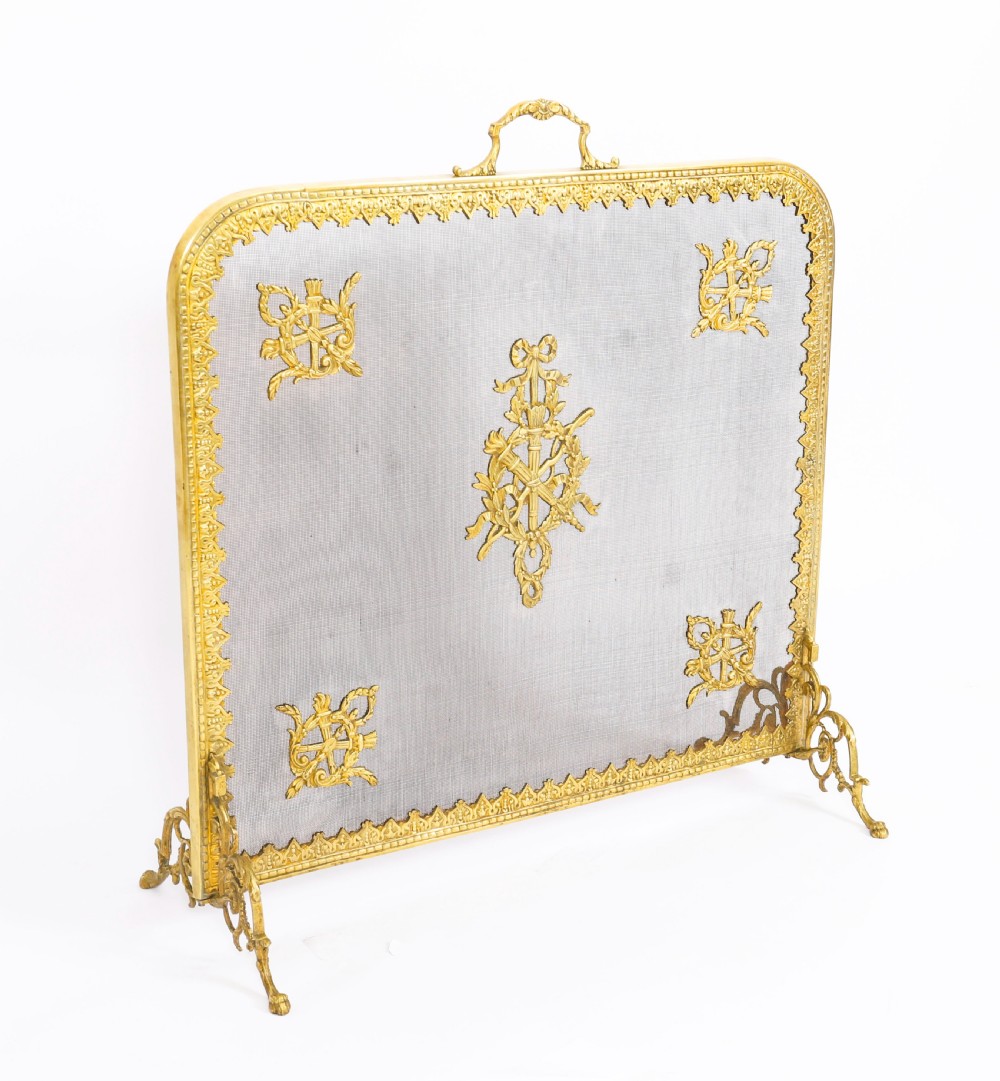 A 19th-century French Empire Revival gilt bronze fire screen featuring fine wire mesh adorned with cast classical trophy mounts, a top handle, and scrolled feet.