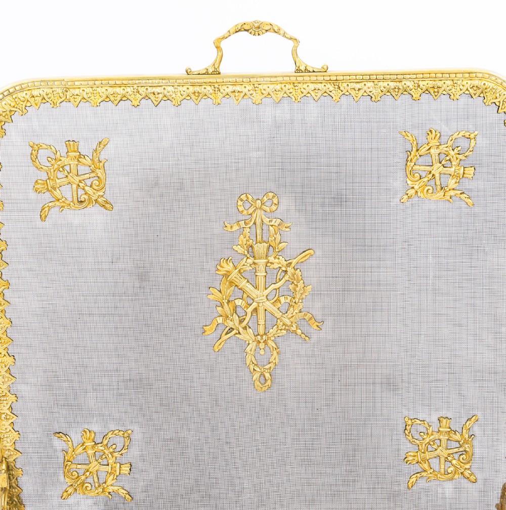 A 19th-century French Empire Revival gilt bronze fire screen featuring fine wire mesh adorned with cast classical trophy mounts, a top handle, and scrolled feet. View IV