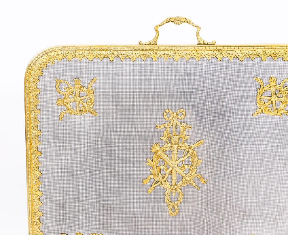 A 19th-century French Empire Revival gilt bronze fire screen featuring fine wire mesh adorned with cast classical trophy mounts, a top handle, and scrolled feet. View V