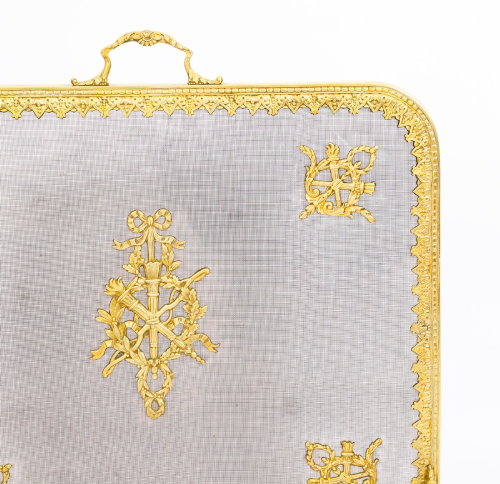 A 19th-century French Empire Revival gilt bronze fire screen featuring fine wire mesh adorned with cast classical trophy mounts, a top handle, and scrolled feet. View VI