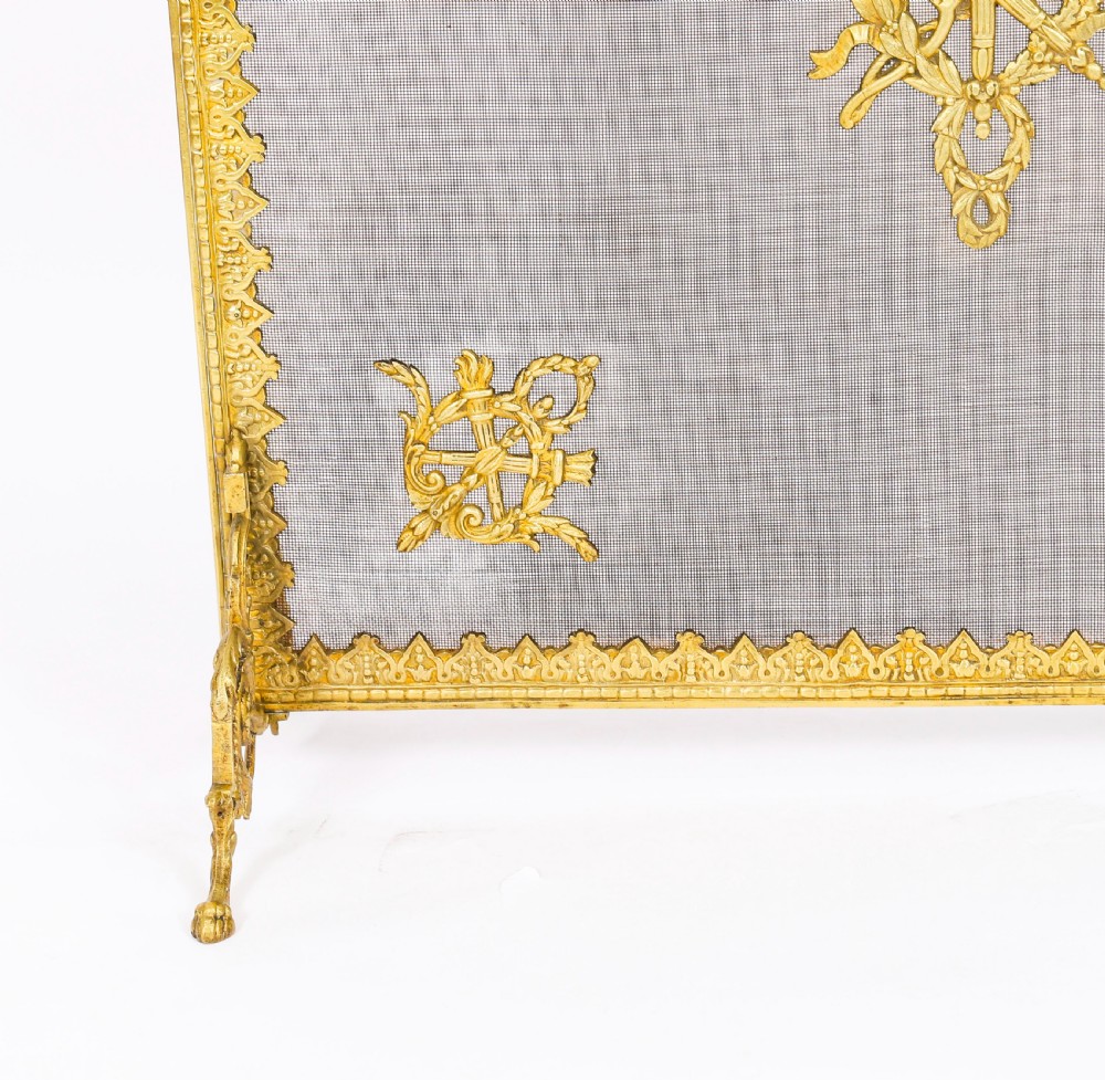 A 19th-century French Empire Revival gilt bronze fire screen featuring fine wire mesh adorned with cast classical trophy mounts, a top handle, and scrolled feet. View X