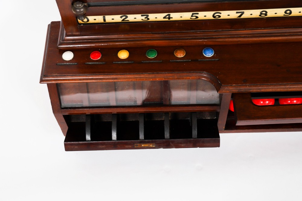 A Victorian mahogany life pool scoreboard featuring a central slate panel, brass slider indicators, coloured markers, and a lower glazed cabinet displaying billiard balls. View XII