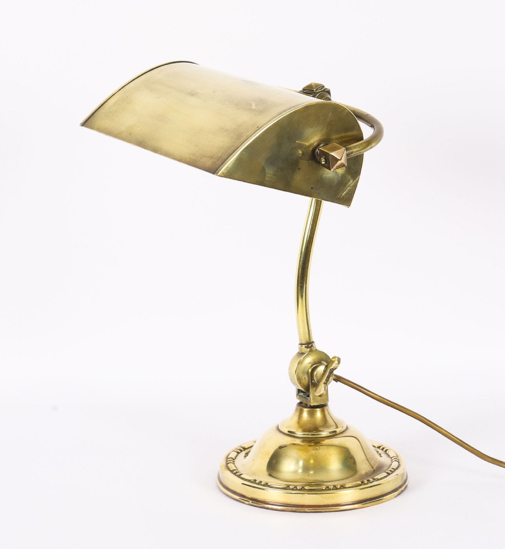 An Art Deco articulated brass desk lamp featuring a curved adjustable arm, a rectangular brass shade, and a moulded circular base.