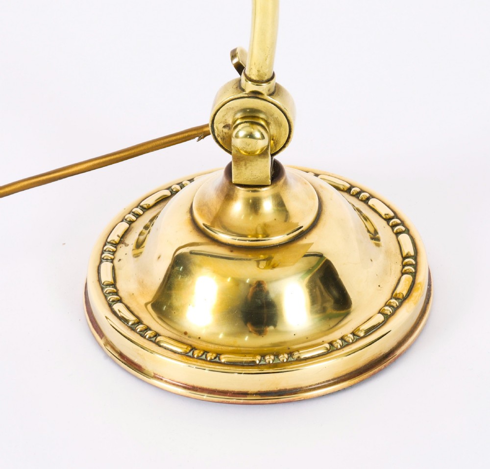 An Art Deco articulated brass desk lamp featuring a curved adjustable arm, a rectangular brass shade, and a moulded circular base. View X