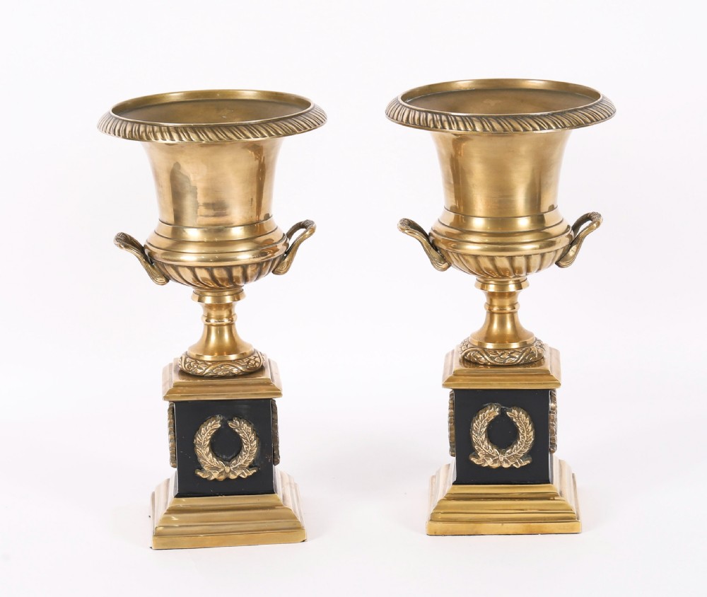 A pair of 19th-century Neoclassical brass Grand Tour campana urns mounted on square black plinths with gilded laurel wreath embellishments.