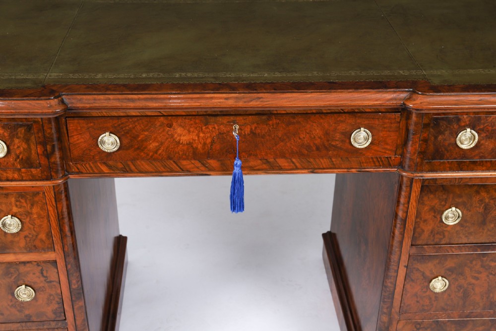 A nineteenth-century Victorian burr walnut twin pedestal desk featuring a green leather writing insert, brass ring handles, and multiple drawers. View VI