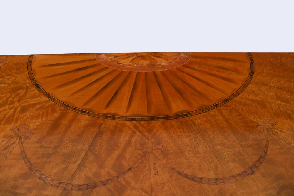 A semicircular antique satinwood demilune cabinet featuring urn and swag marquetry inlays, a top drawer with a blue tassel key, and slender tapered legs. View XII
