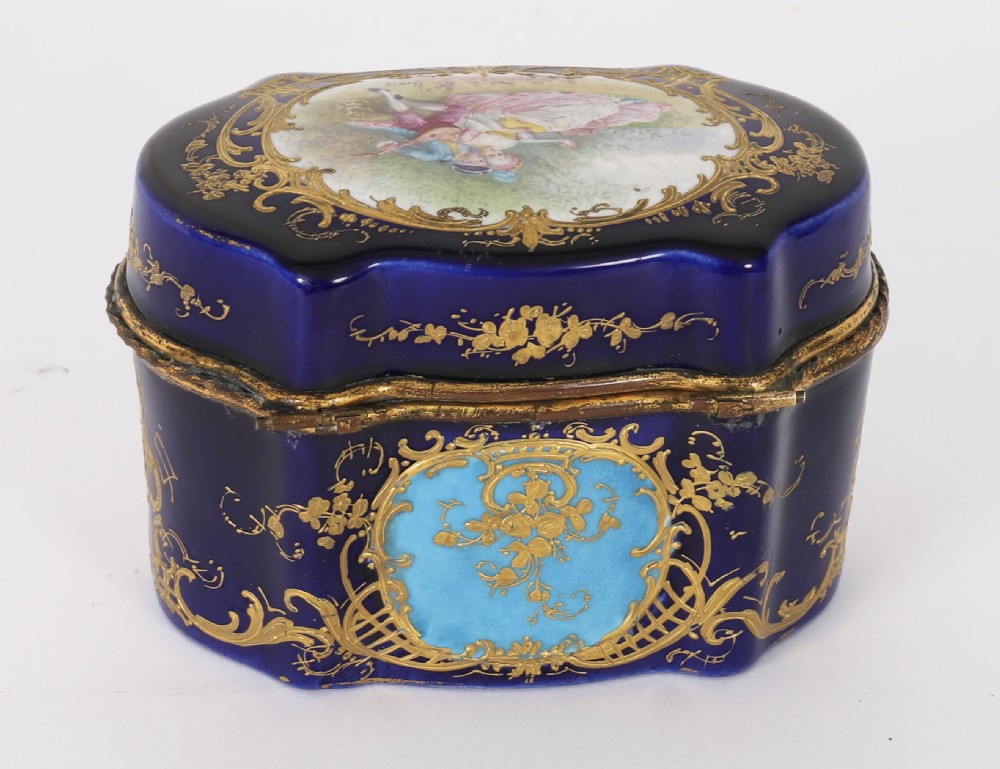 A serpentine cobalt blue porcelain casket featuring gilt-bronze mounts, hand-painted romantic scenes, floral reserves, and heavy gold scrollwork. View X