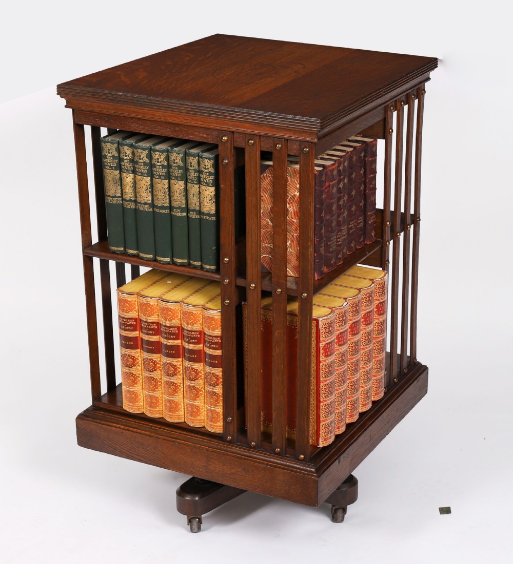 A two-tier Victorian dark oak revolving bookcase with vertical side slats and brass studs, raised on a quadruped base with metal castors.