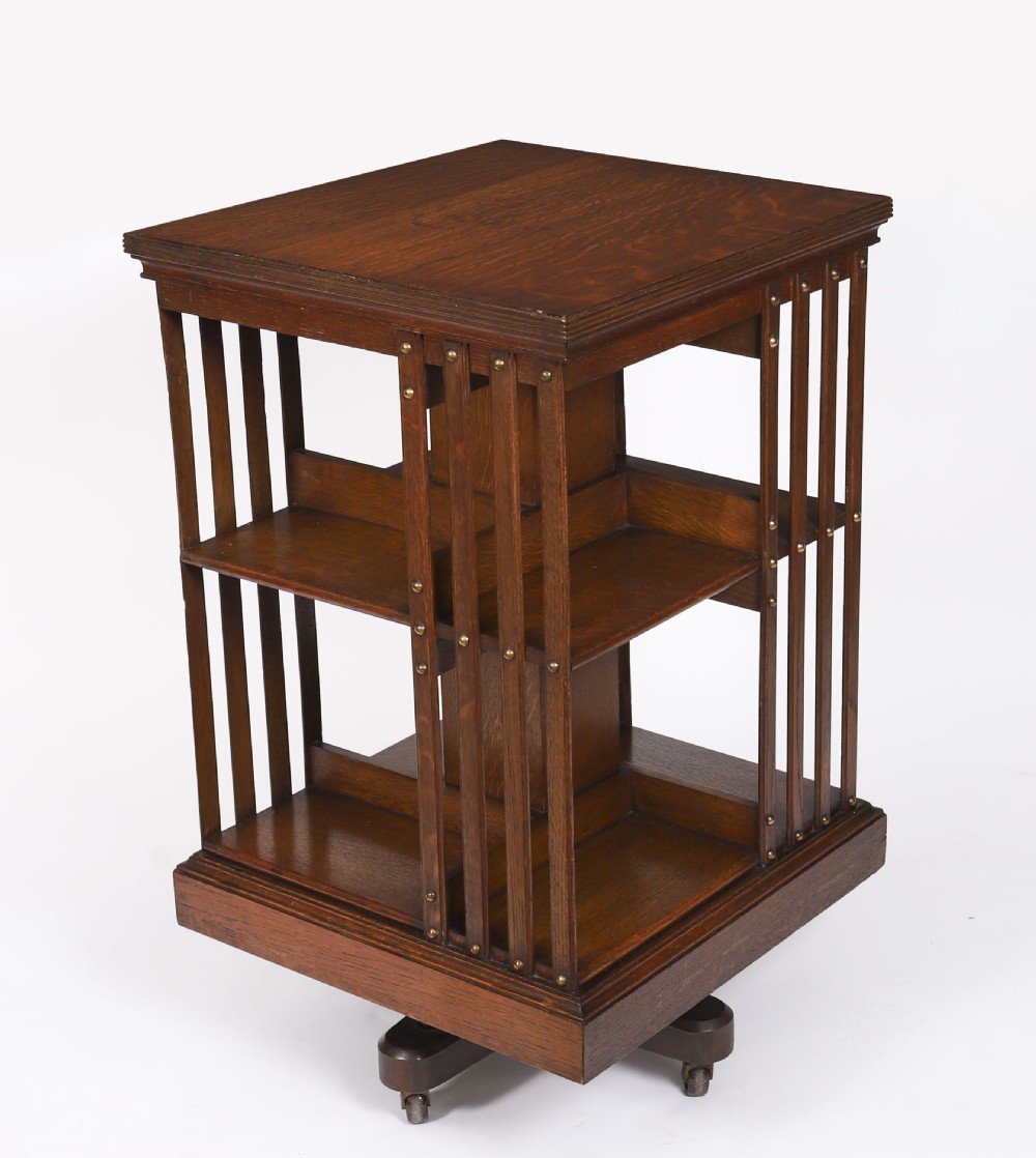A two-tier Victorian dark oak revolving bookcase with vertical side slats and brass studs, raised on a quadruped base with metal castors. View II