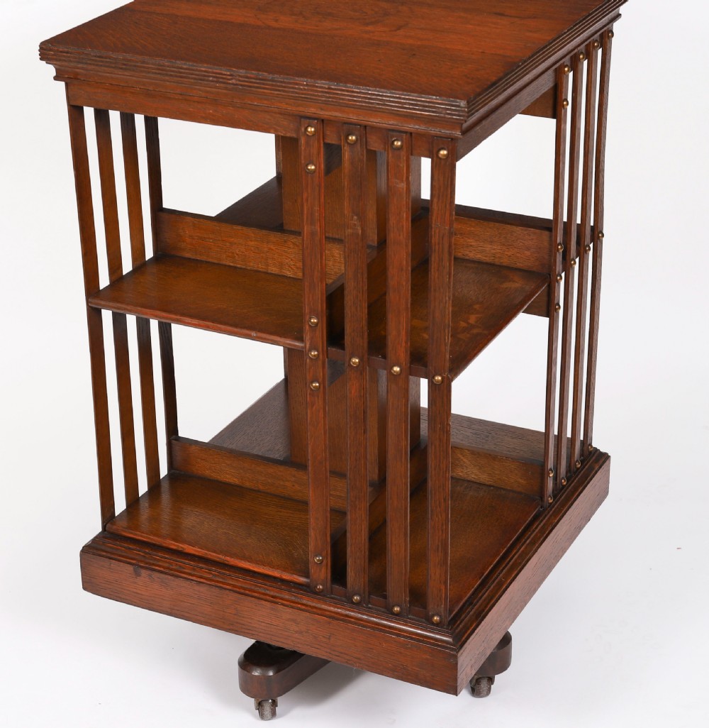 A two-tier Victorian dark oak revolving bookcase with vertical side slats and brass studs, raised on a quadruped base with metal castors. View IV