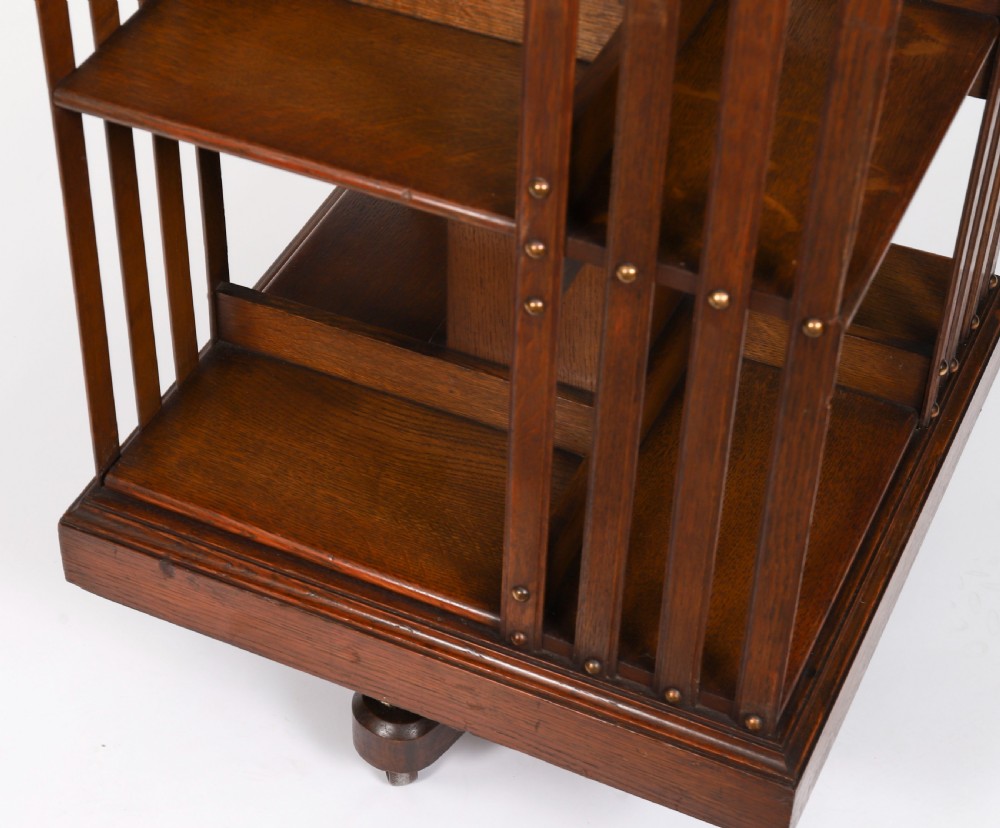 A two-tier Victorian dark oak revolving bookcase with vertical side slats and brass studs, raised on a quadruped base with metal castors. View VI