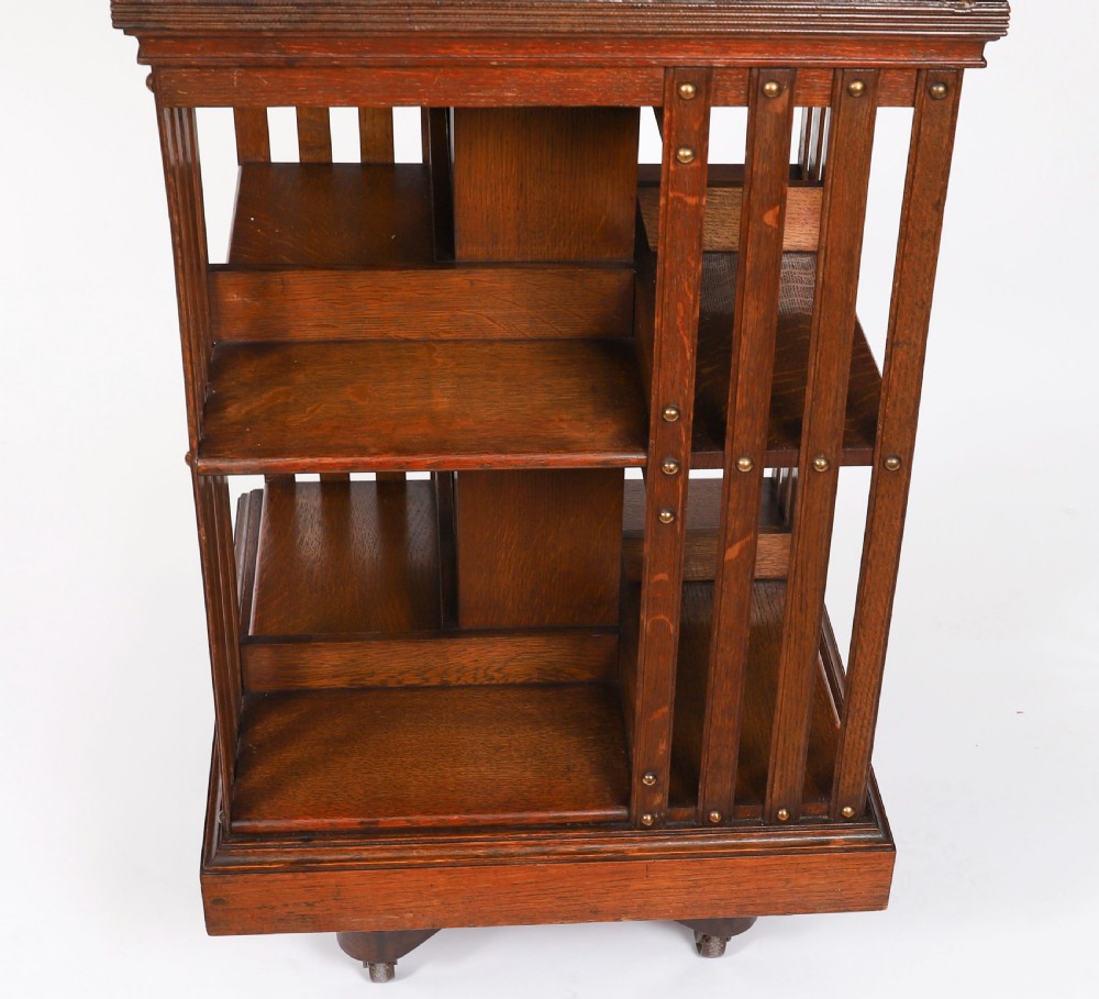 A two-tier Victorian dark oak revolving bookcase with vertical side slats and brass studs, raised on a quadruped base with metal castors. View VII