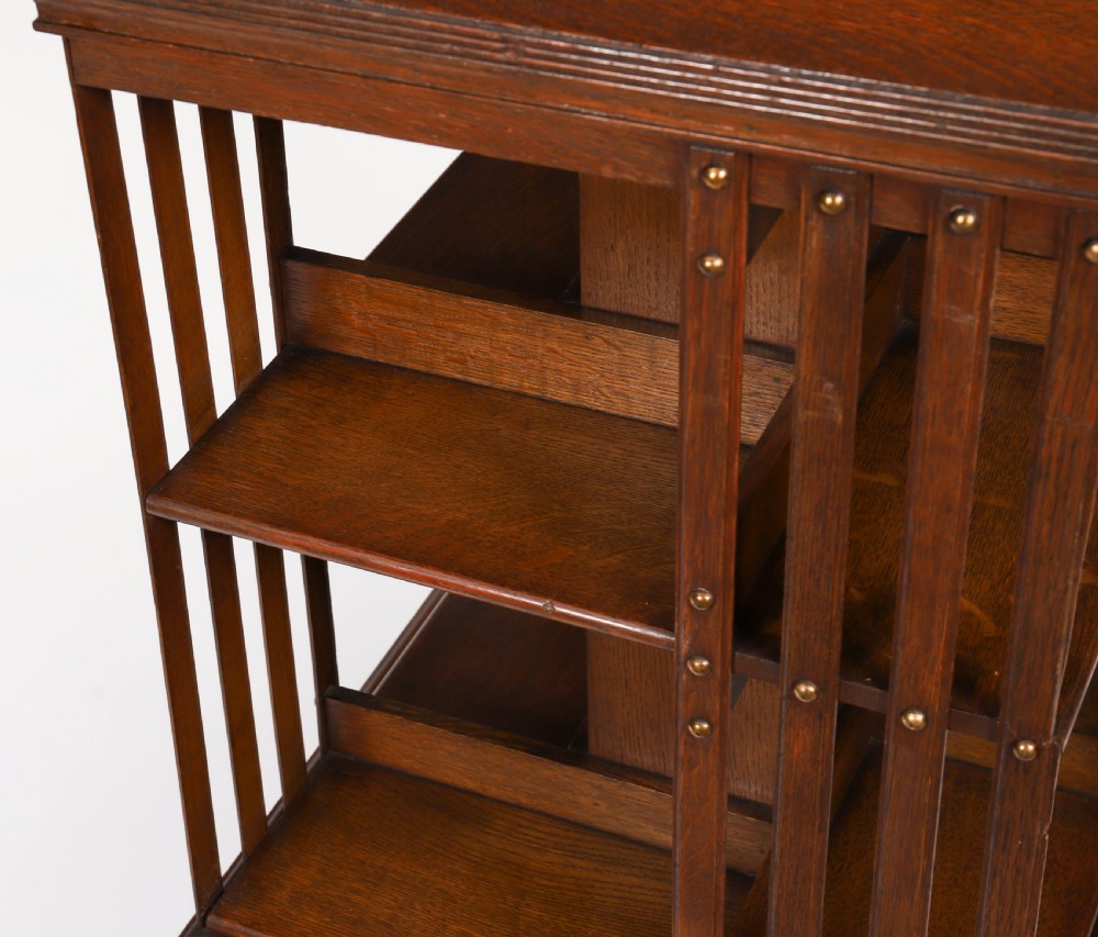 A two-tier Victorian dark oak revolving bookcase with vertical side slats and brass studs, raised on a quadruped base with metal castors. View IX
