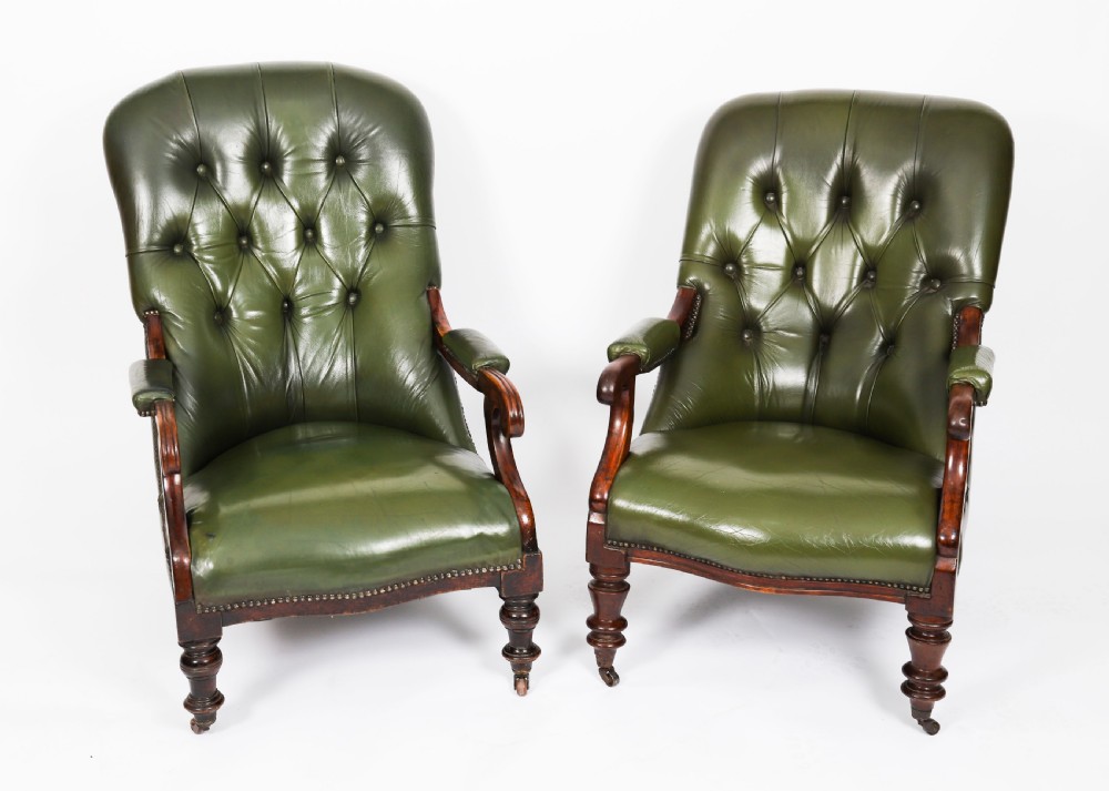 A pair of Victorian 19th-century armchairs upholstered in deep-buttoned green leather with dark mahogany frames and turned front legs on castors.