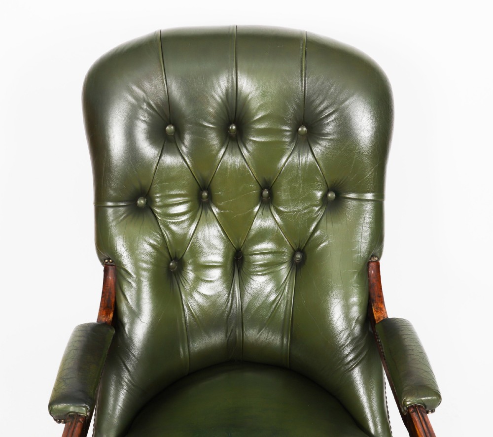 A pair of Victorian 19th-century armchairs upholstered in deep-buttoned green leather with dark mahogany frames and turned front legs on castors. View V