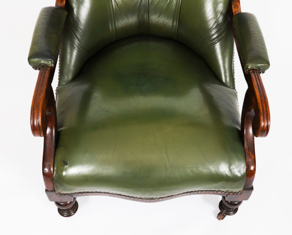 A pair of Victorian 19th-century armchairs upholstered in deep-buttoned green leather with dark mahogany frames and turned front legs on castors. View VII