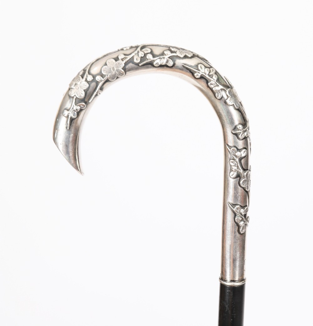 A 19th-century walking cane featuring a curved silver crook handle embossed with cherry blossom motifs attached to a dark wood shaft.