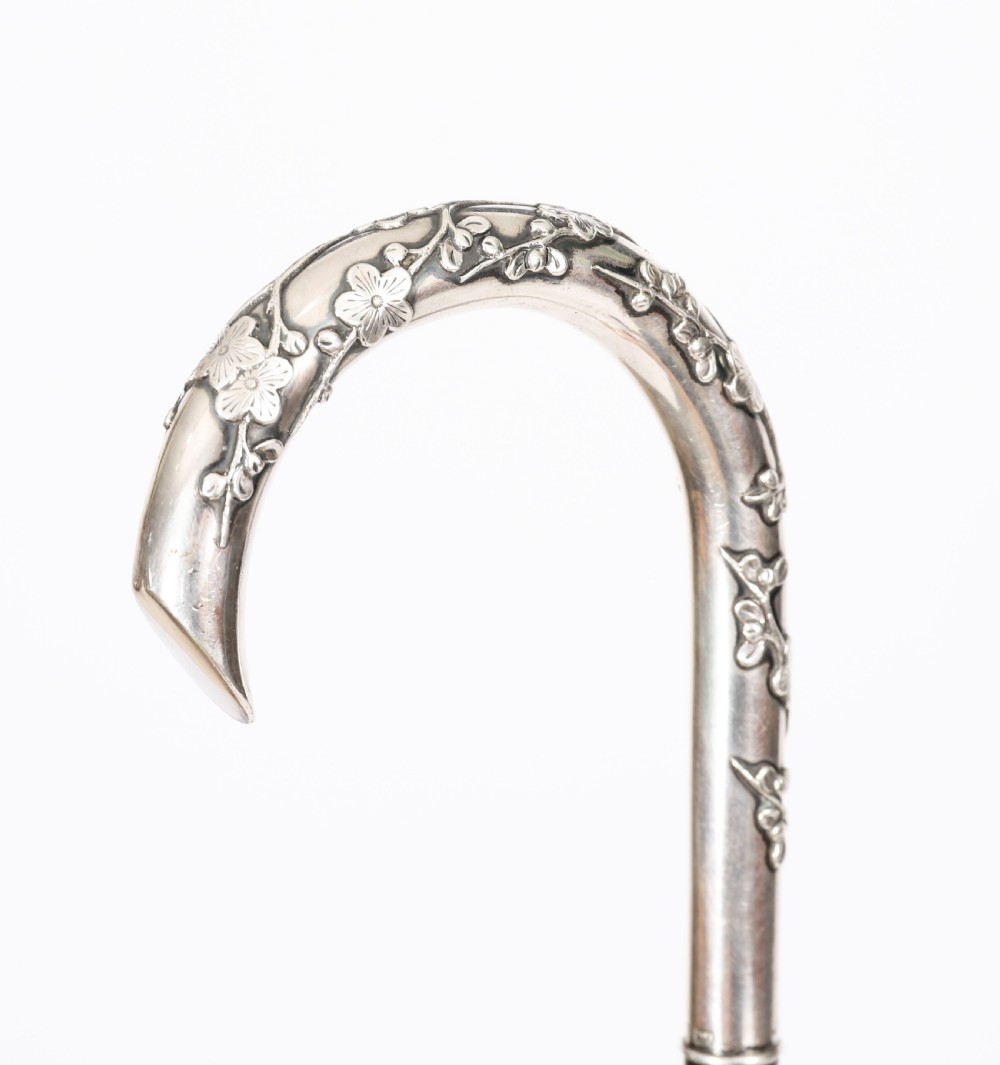 A 19th-century walking cane featuring a curved silver crook handle embossed with cherry blossom motifs attached to a dark wood shaft. View VI