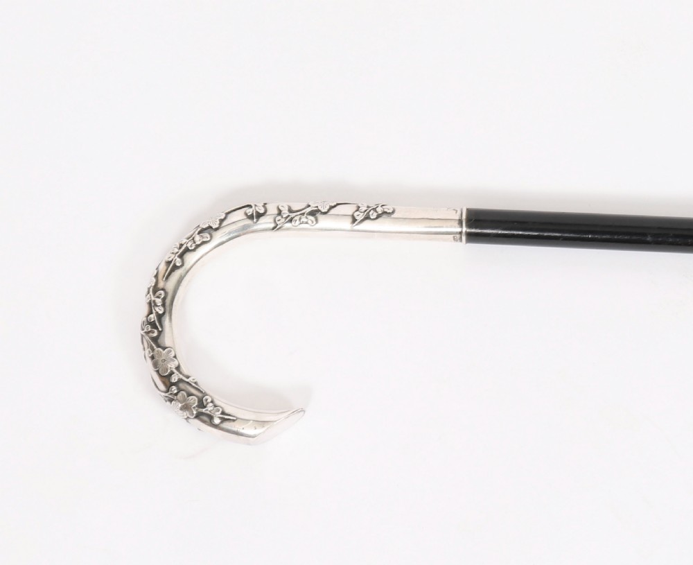 A 19th-century walking cane featuring a curved silver crook handle embossed with cherry blossom motifs attached to a dark wood shaft. View X