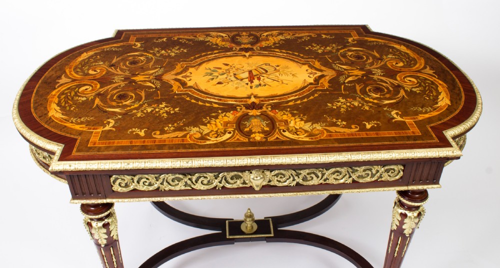 An antique French bureau plat writing table featuring detailed floral marquetry inlays, decorative gilt-bronze ormolu mounts, turned legs, and an X-frame stretcher. View IV