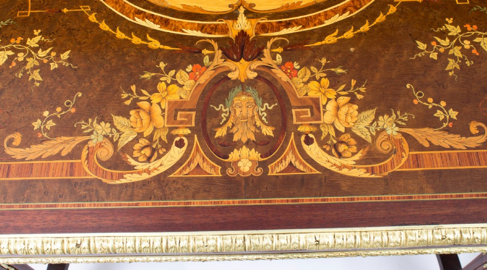 An antique French bureau plat writing table featuring detailed floral marquetry inlays, decorative gilt-bronze ormolu mounts, turned legs, and an X-frame stretcher. View V