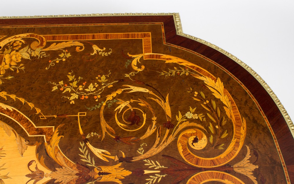 An antique French bureau plat writing table featuring detailed floral marquetry inlays, decorative gilt-bronze ormolu mounts, turned legs, and an X-frame stretcher. View X