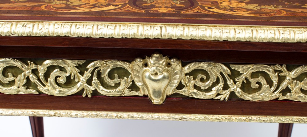 An antique French bureau plat writing table featuring detailed floral marquetry inlays, decorative gilt-bronze ormolu mounts, turned legs, and an X-frame stretcher. View XI