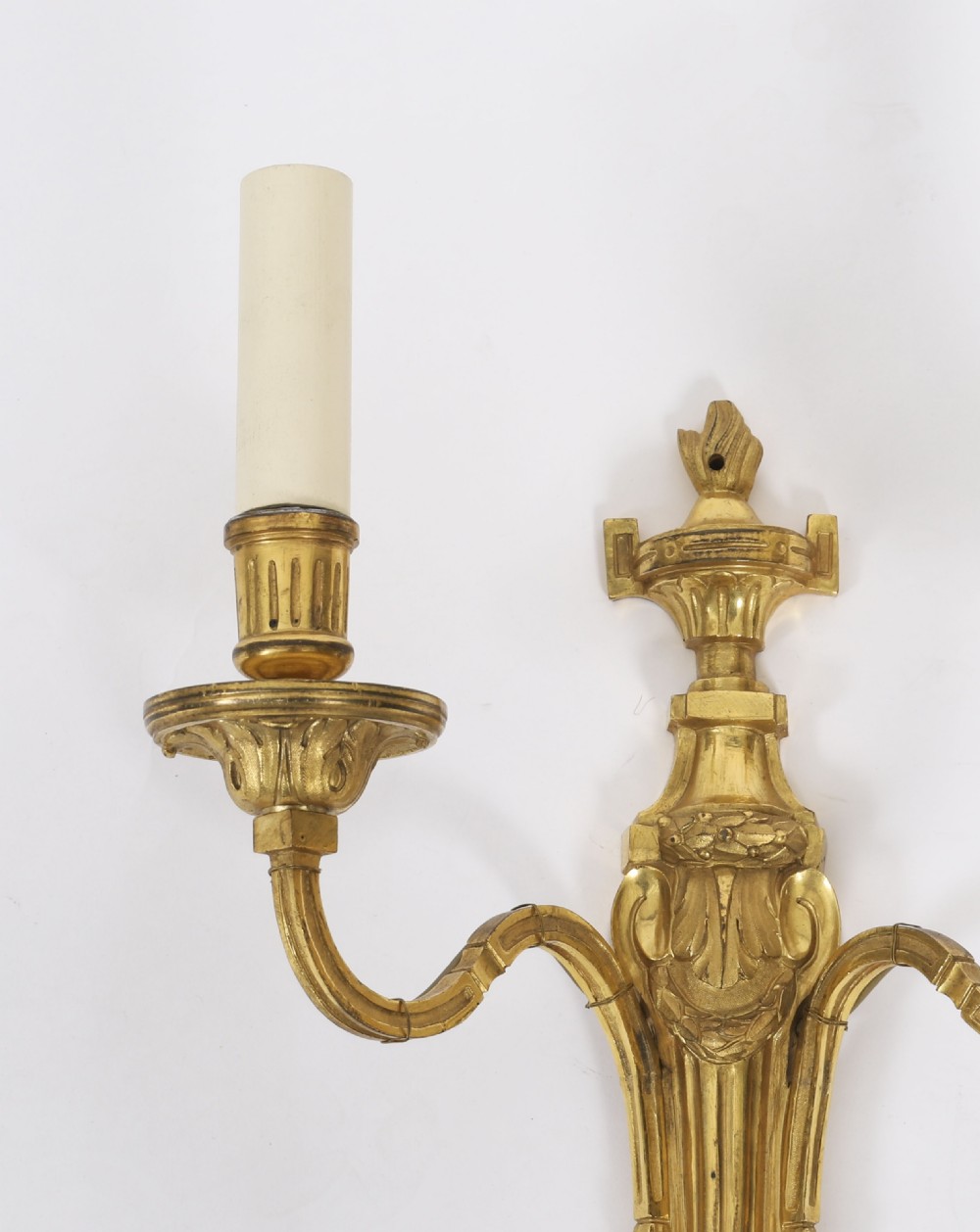 A pair of antique French Louis XVI style two-branch ormolu wall lights with fluted backplates and cream candle sleeves. View IV