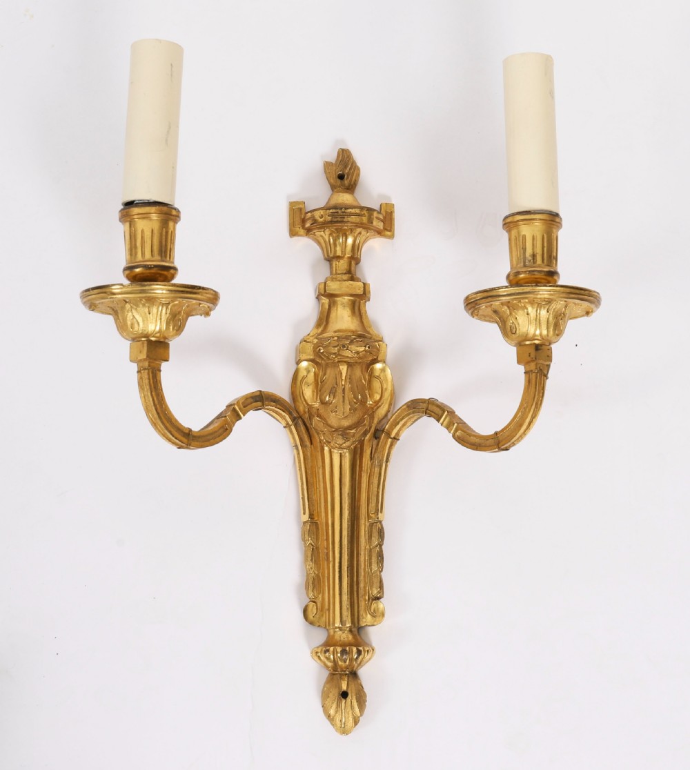 A pair of antique French Louis XVI style two-branch ormolu wall lights with fluted backplates and cream candle sleeves. View V
