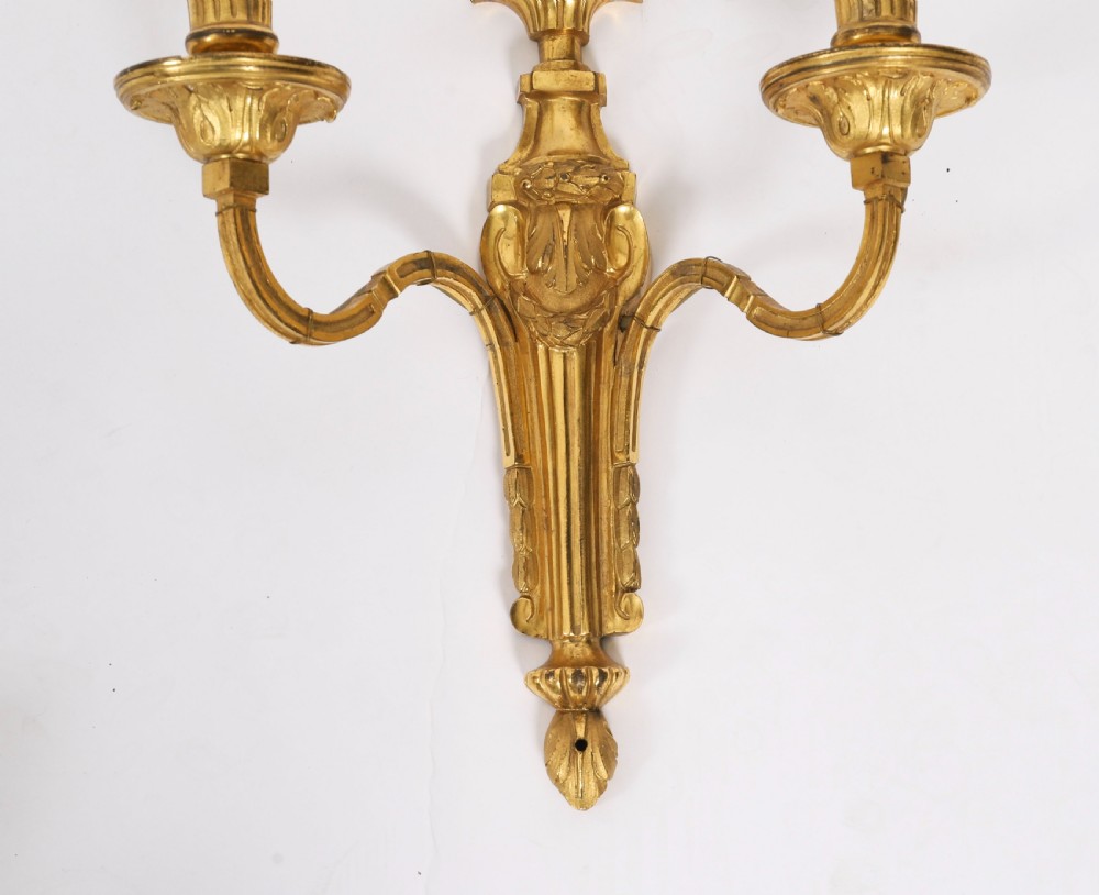 A pair of antique French Louis XVI style two-branch ormolu wall lights with fluted backplates and cream candle sleeves. View VII