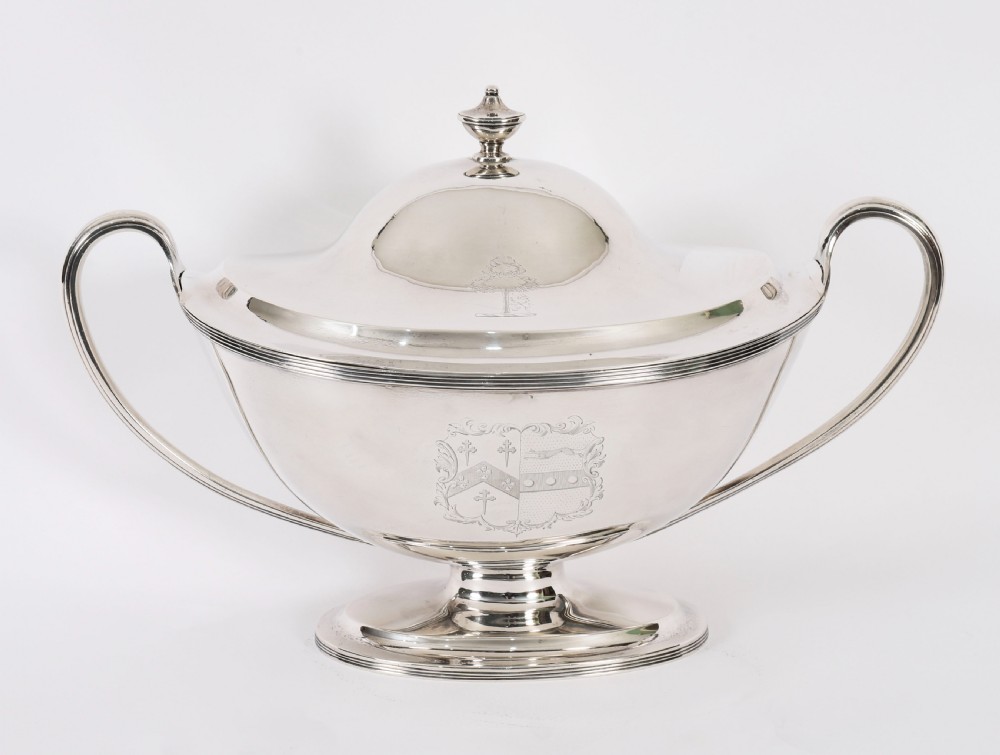 A George III sterling silver tureen with two looped handles, a domed lid, a pedestal base, and an engraved heraldic crest. View II