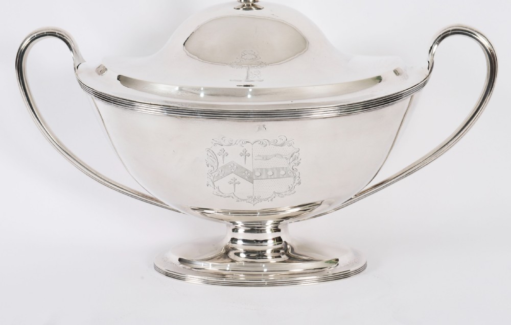 A George III sterling silver tureen with two looped handles, a domed lid, a pedestal base, and an engraved heraldic crest. View III