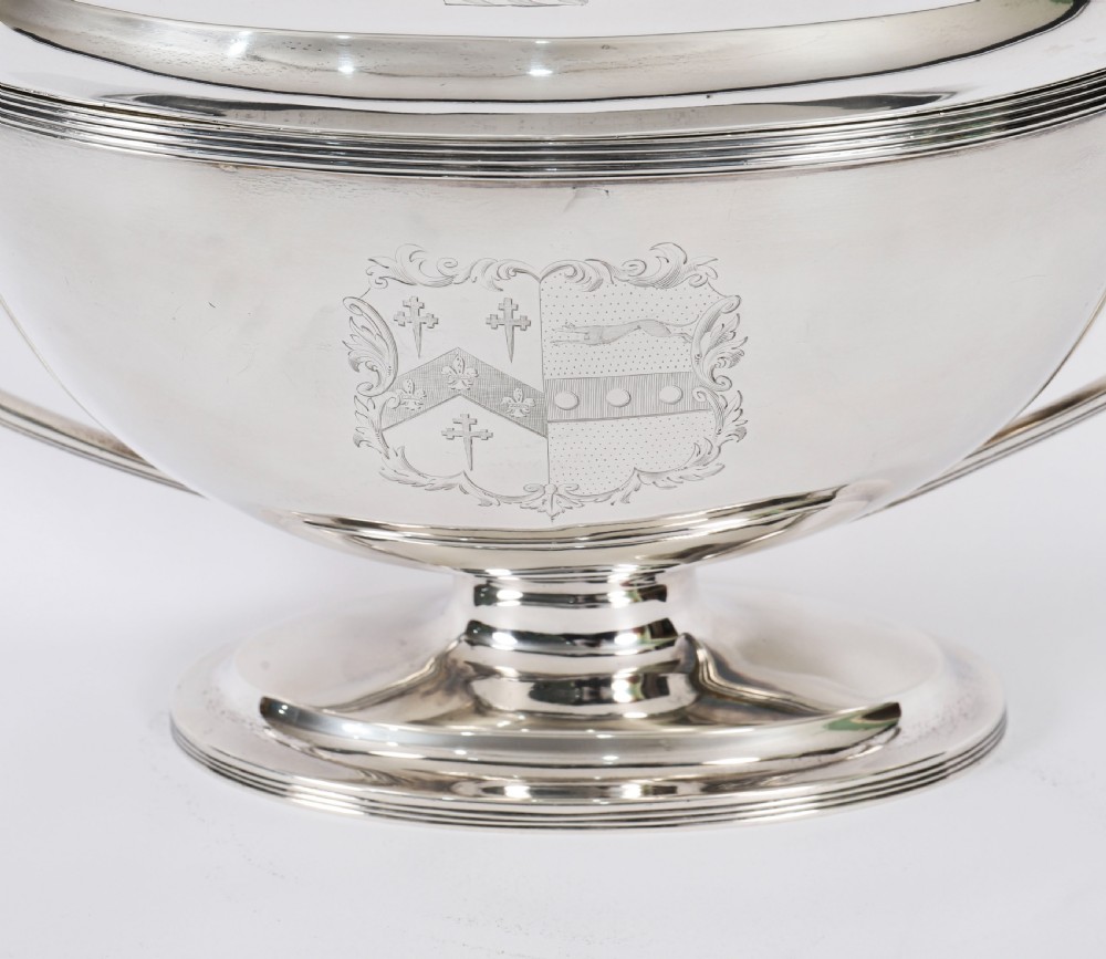 A George III sterling silver tureen with two looped handles, a domed lid, a pedestal base, and an engraved heraldic crest. View VI