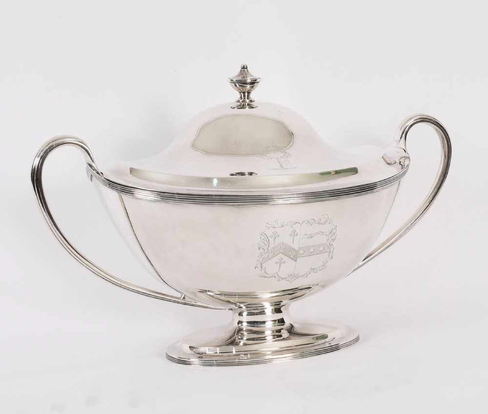A George III sterling silver tureen with two looped handles, a domed lid, a pedestal base, and an engraved heraldic crest. View IX