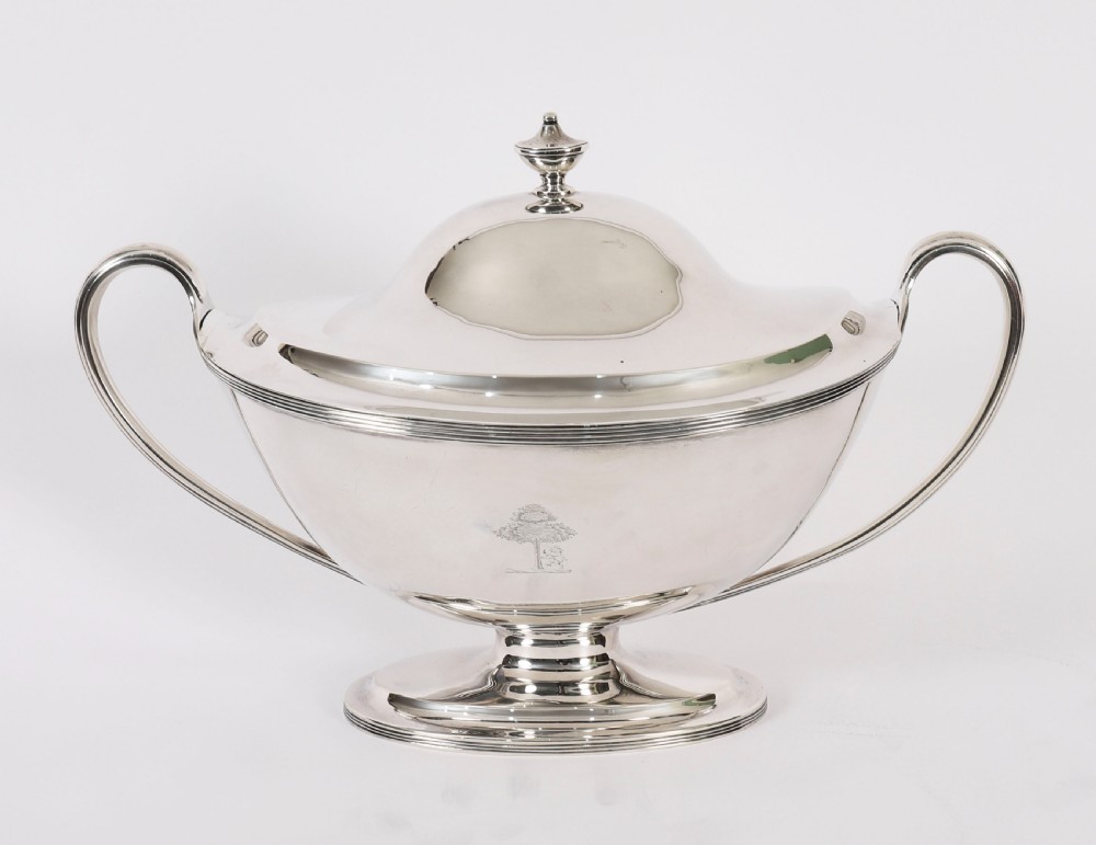 A George III sterling silver tureen with two looped handles, a domed lid, a pedestal base, and an engraved heraldic crest. View X