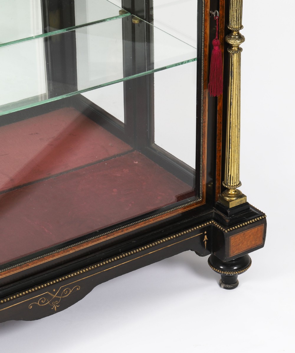 A Victorian ebonised and amboyna wood pier display cabinet featuring glass doors, interior glass shelves, and gilded brass mounts. View X