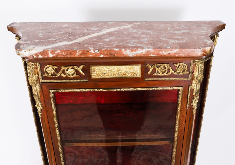 A 19th-century French Louis Revival vitrine cabinet featuring a marble top, glazed glass sides and door, floral marquetry panels, and ornate gilt bronze mounts. View VI