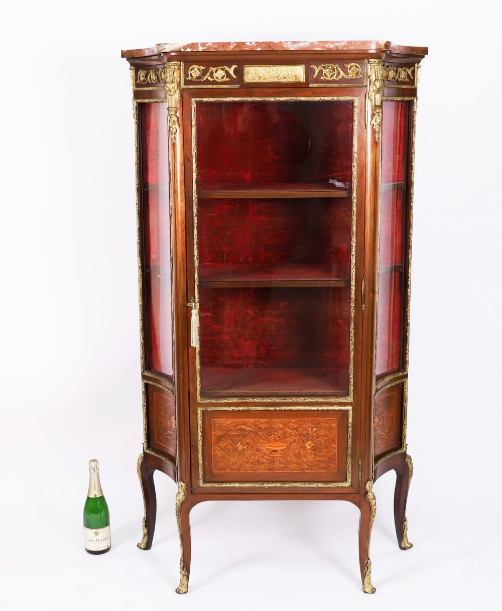 A 19th-century French Louis Revival vitrine cabinet featuring a marble top, glazed glass sides and door, floral marquetry panels, and ornate gilt bronze mounts. View XVII