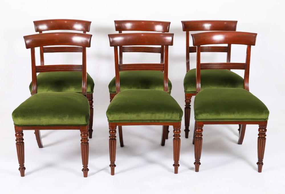 A set of six Regency mahogany dining chairs featuring curved bar top rails, reeded front legs, and green velvet seats.