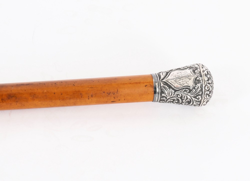 An antique walking stick featuring an elaborately chased silver pommel handle with foliate motifs mounted on a smooth light timber shaft. View IV