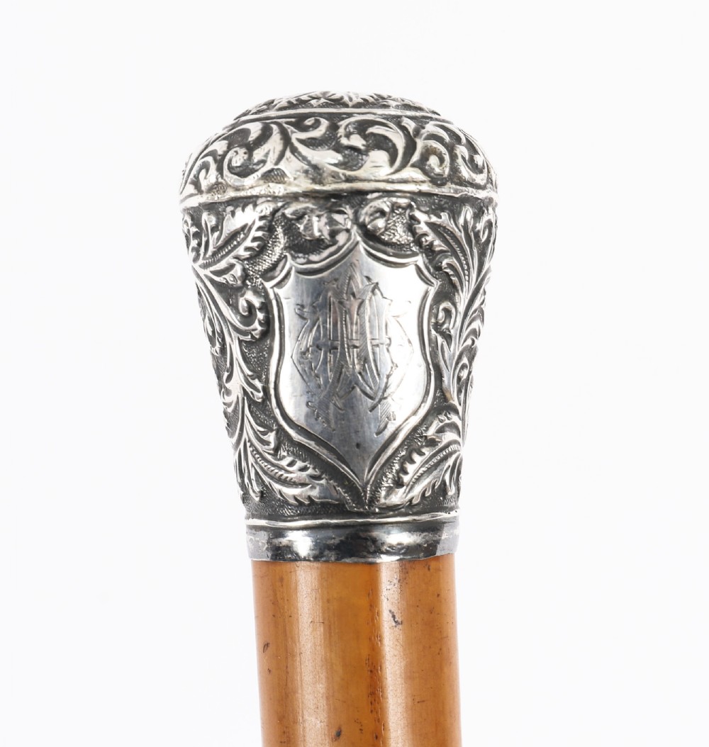 An antique walking stick featuring an elaborately chased silver pommel handle with foliate motifs mounted on a smooth light timber shaft. View XI