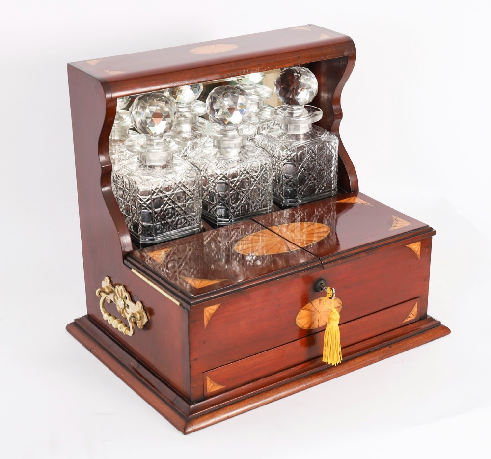 A 19th-century inlaid satinwood and mahogany tantalus containing three cut crystal decanters with faceted stoppers, a mirrored back interior, and a lower fold-out compartment with oval marquetry paterae.