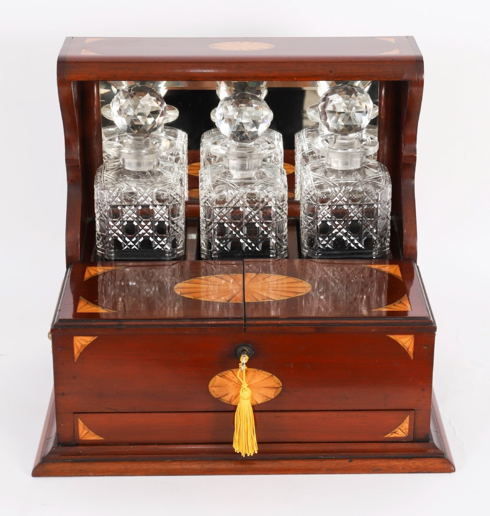 A 19th-century inlaid satinwood and mahogany tantalus containing three cut crystal decanters with faceted stoppers, a mirrored back interior, and a lower fold-out compartment with oval marquetry paterae. View III