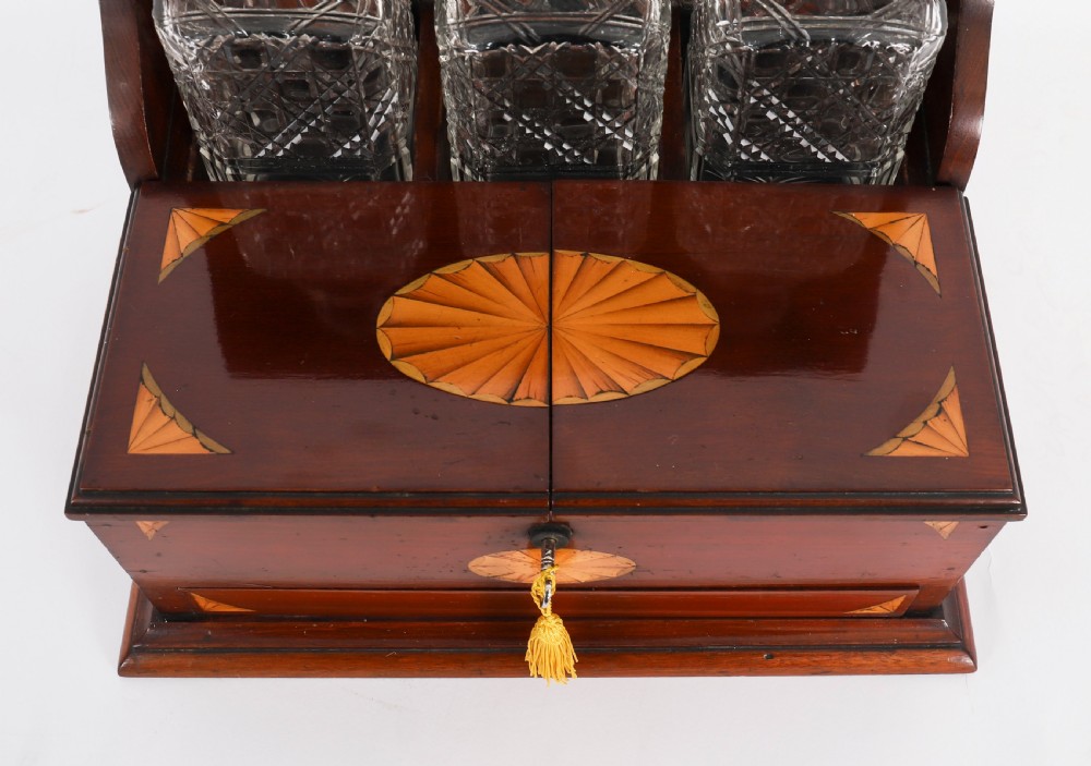 A 19th-century inlaid satinwood and mahogany tantalus containing three cut crystal decanters with faceted stoppers, a mirrored back interior, and a lower fold-out compartment with oval marquetry paterae. View IV