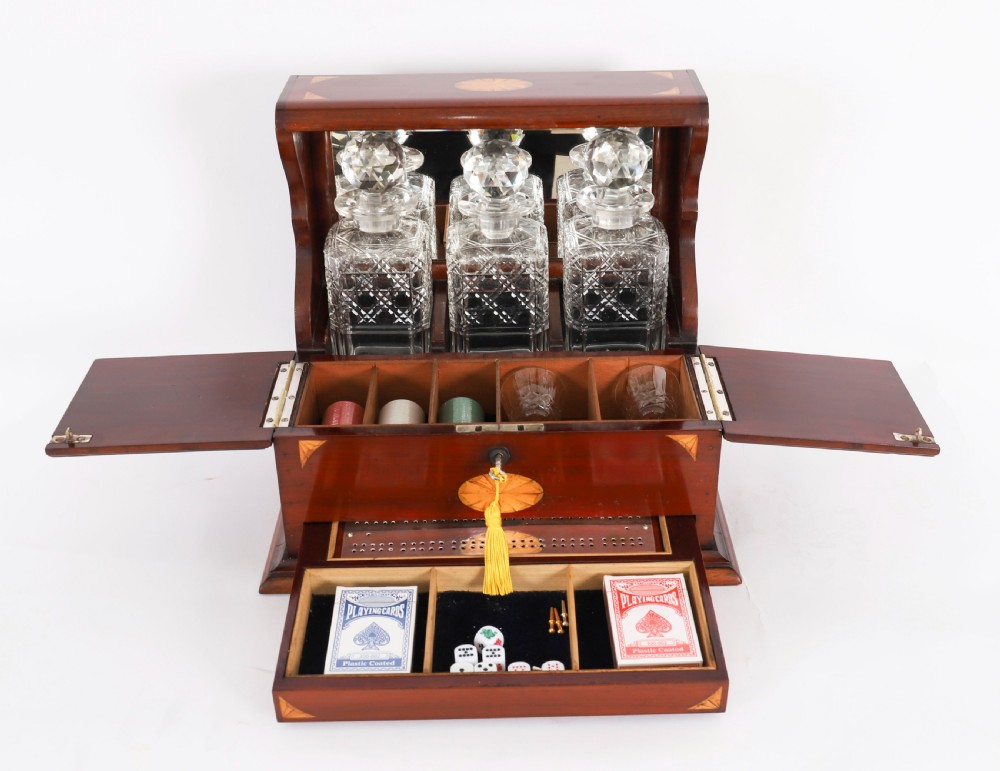 A 19th-century inlaid satinwood and mahogany tantalus containing three cut crystal decanters with faceted stoppers, a mirrored back interior, and a lower fold-out compartment with oval marquetry paterae. View X
