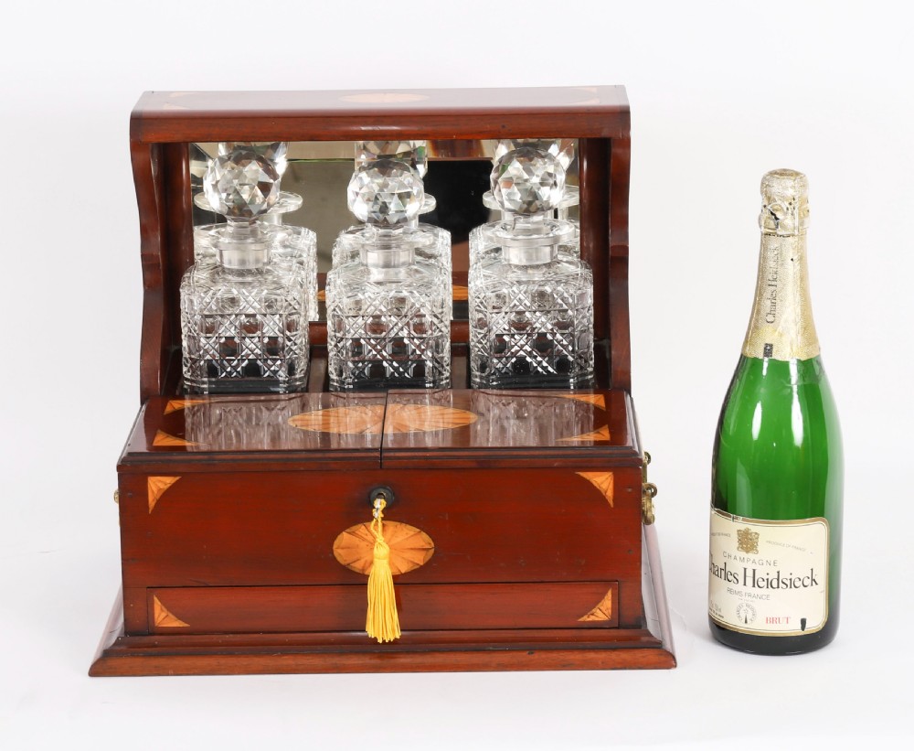 A 19th-century inlaid satinwood and mahogany tantalus containing three cut crystal decanters with faceted stoppers, a mirrored back interior, and a lower fold-out compartment with oval marquetry paterae. View XIX