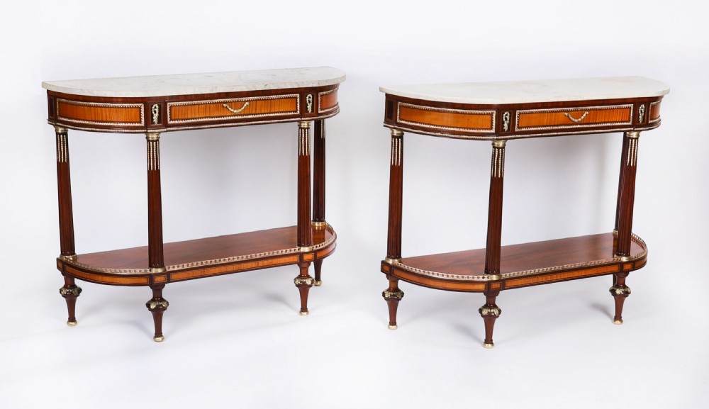 A pair of 19th-century French Louis XVI style demi-lune console tables with white Carrara marble tops, gilt bronze mounts, fluted legs, and undershelves.