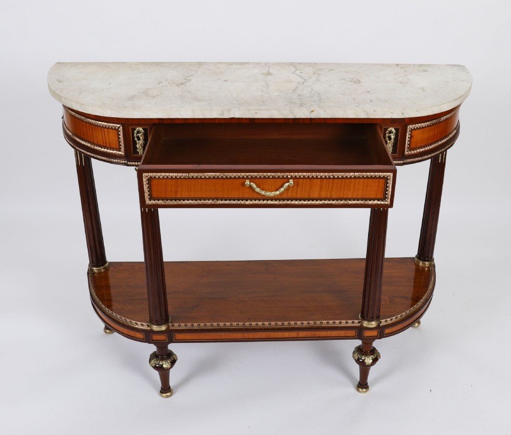 A pair of 19th-century French Louis XVI style demi-lune console tables with white Carrara marble tops, gilt bronze mounts, fluted legs, and undershelves. View IX